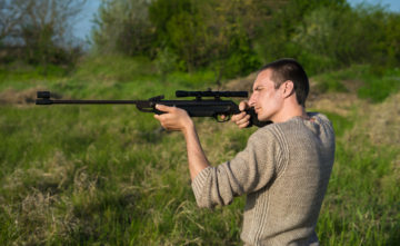 The man takes aim at the target with a sniper strikeball rifle. Selective Focus. Side view