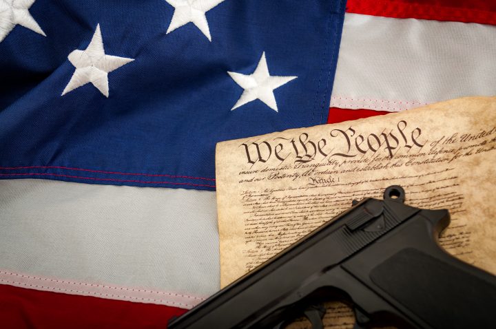 A handgun resting on the Constitution of the United States of America with an American flag in the background.