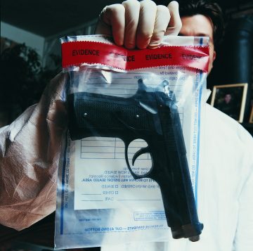 Male Forensic Scientist Holding an Evidence Bag With a Gun Inside