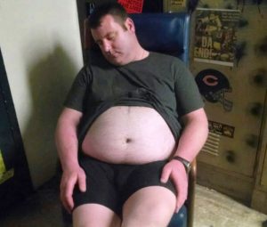 drunk man with large belly passed out in a chair in a locker room