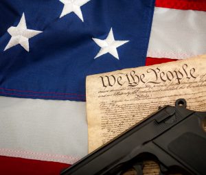 A handgun resting on the Constitution of the United States of America with an American flag in the background.