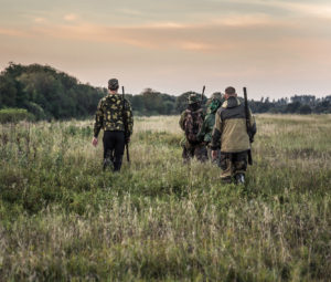 Hunting scene with hunters going through rural field during hunting season in overcast day during sunset with moody sky